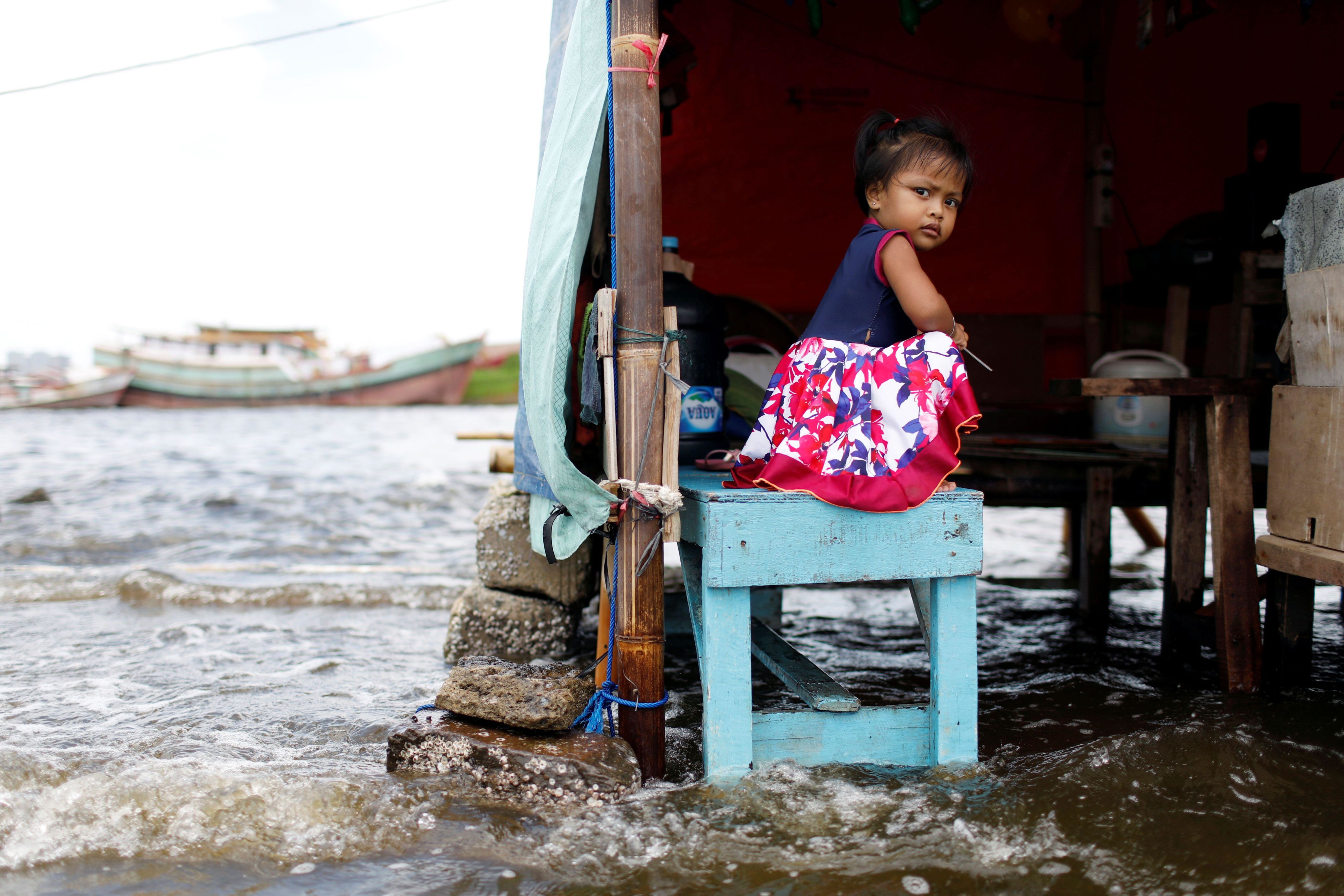 A toddler sits on a bench at Kali Adem port, which is impacted by high tides due to the rising sea level and land subsidence, north of Jakarta, Indonesia