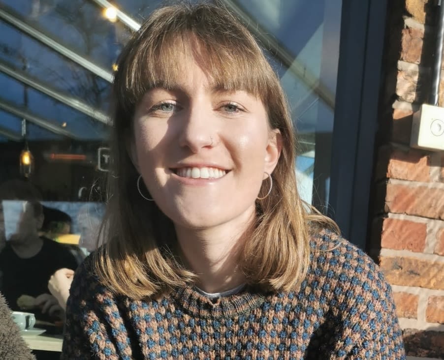Woman with long brown hair and a speckled sweater.
