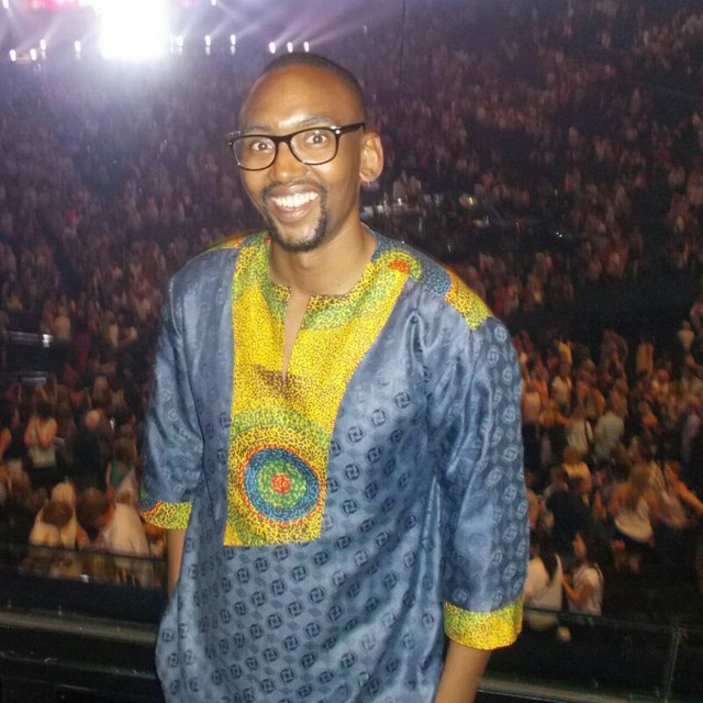 A black man wearing a blue and yellow shirt in an African style.