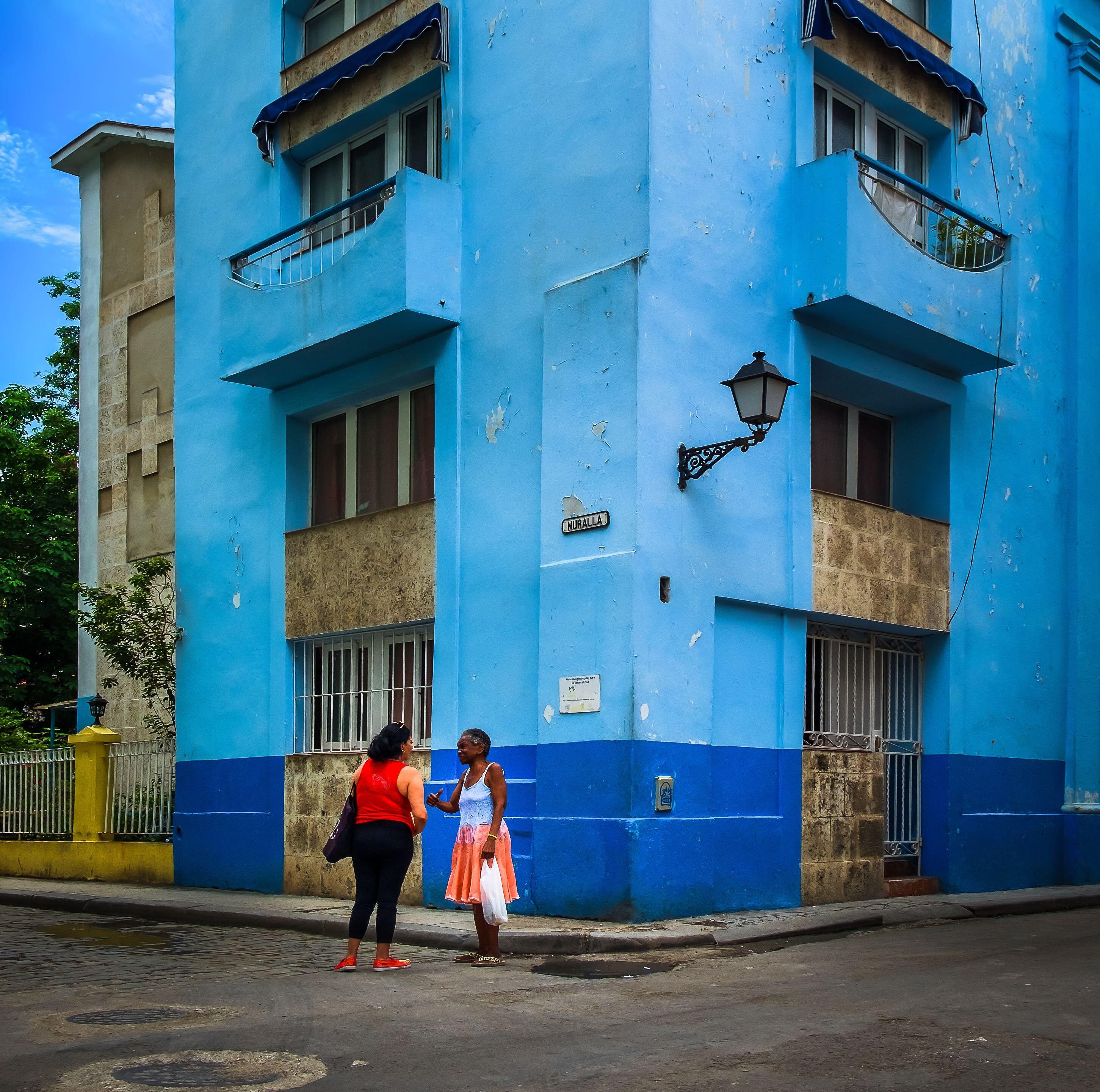 Two women chatting outside a bright blue building in Havana, Cuba.