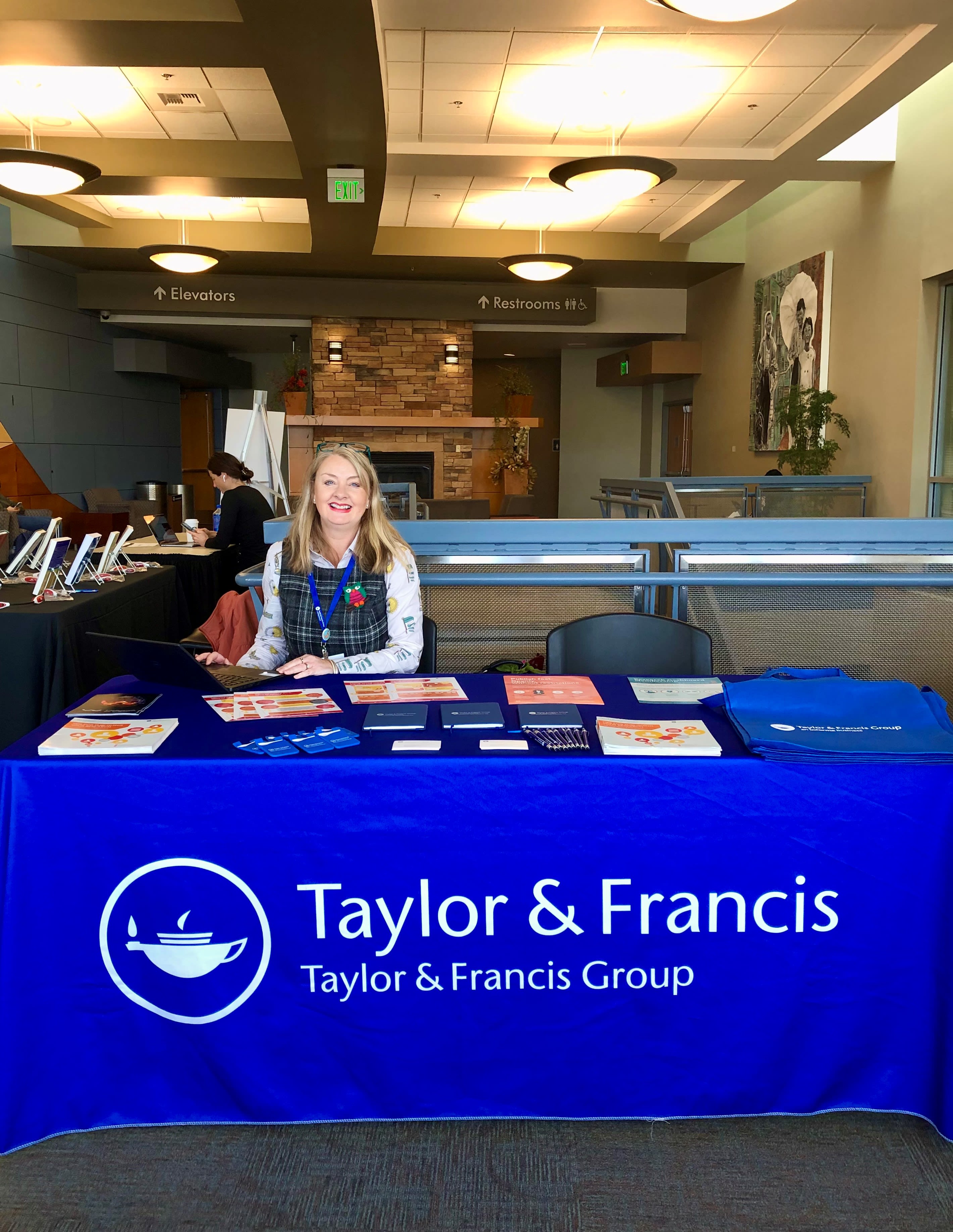 Photo of a woman sitting at a table with a Taylor & Francis banner on it.