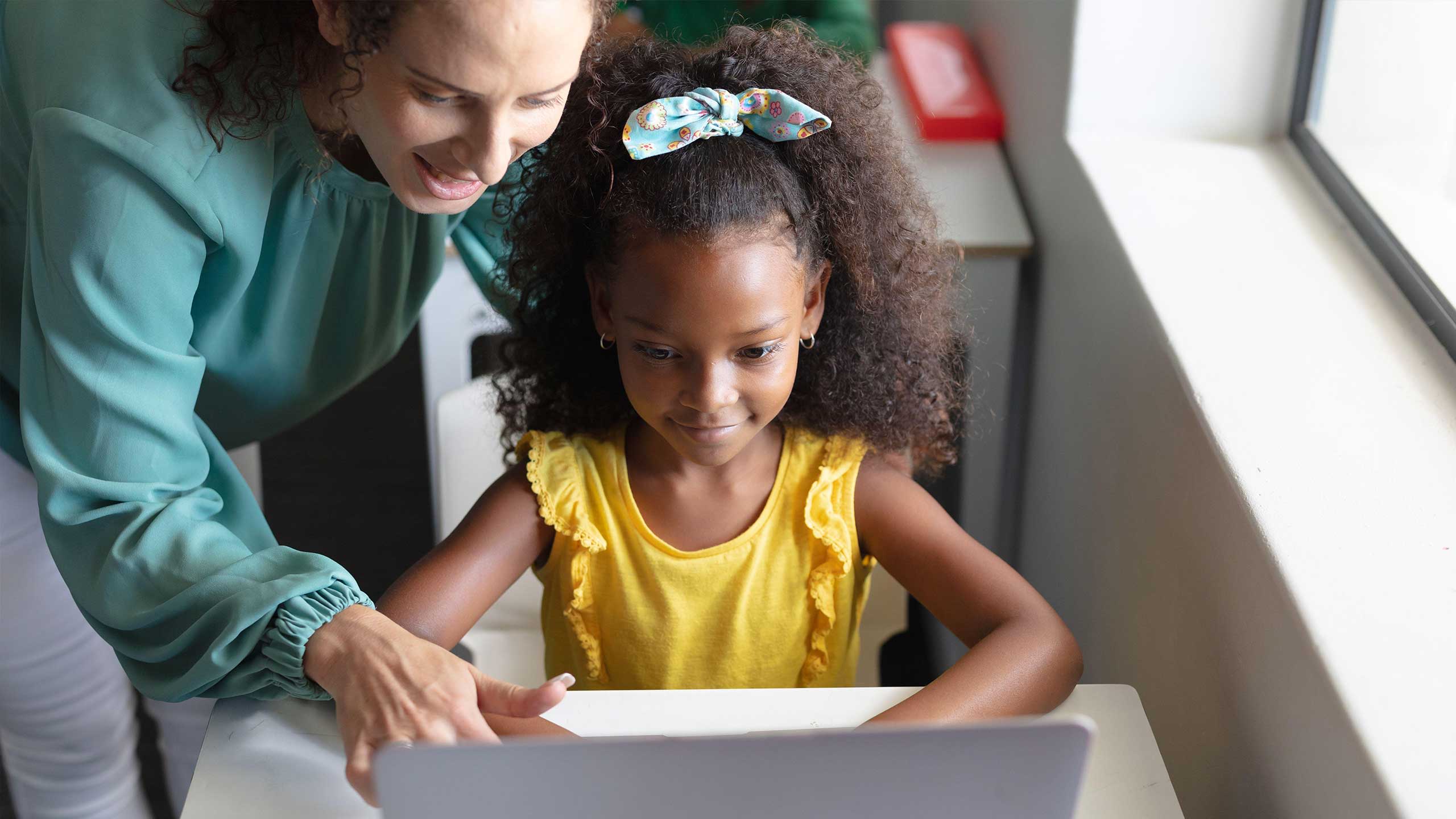 Carer showing young girl how to code on a computer