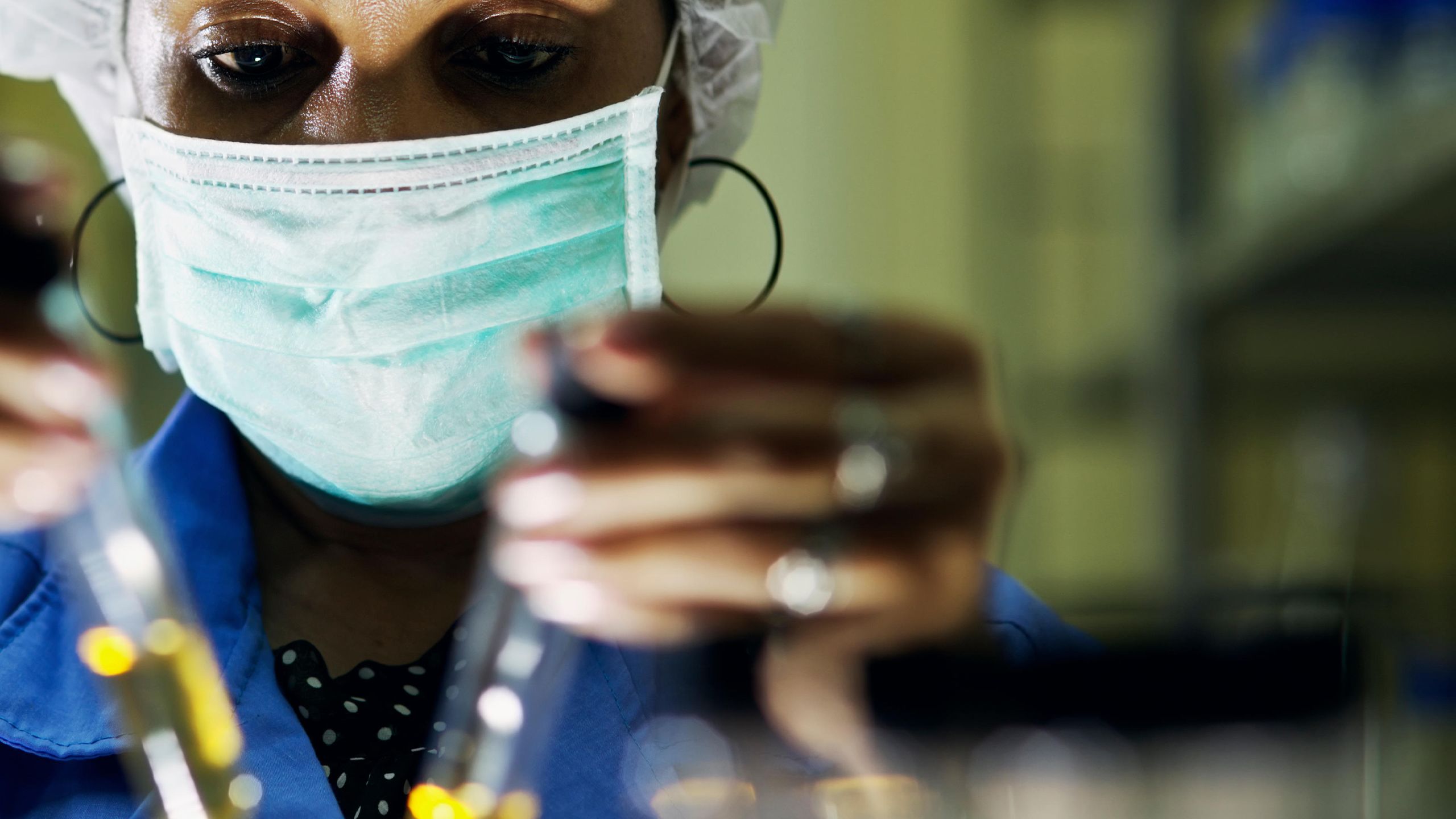 Woman scientist wearing face mask compares samples in a test tube