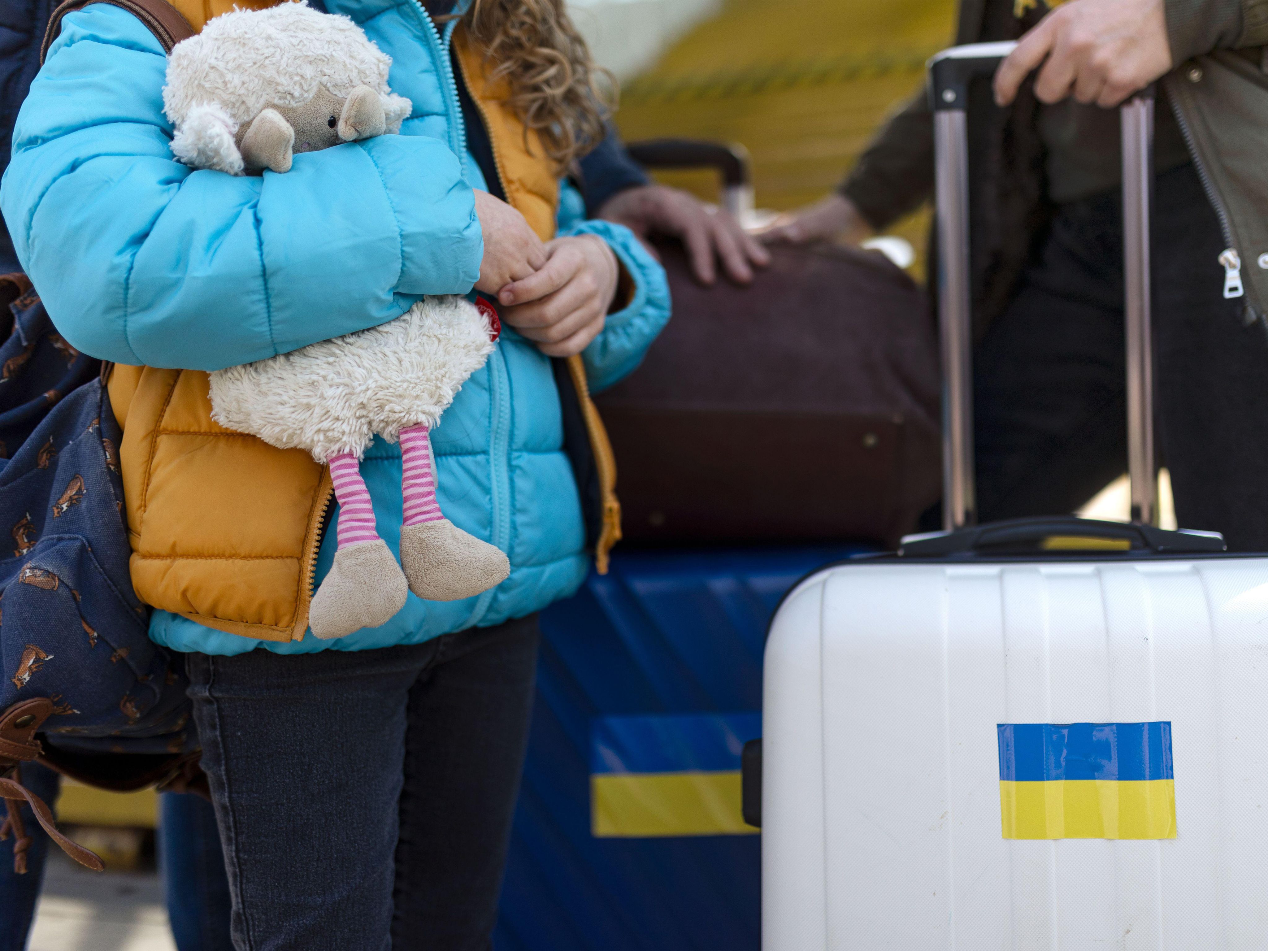 Close up of Ukrainian refugee suit cases and child holding toy
