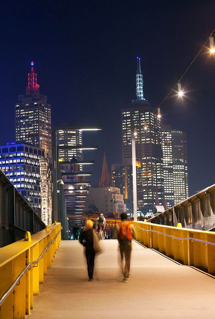 Pedestrians on car-free path in Melbourne, Australia at night with cityscape in background