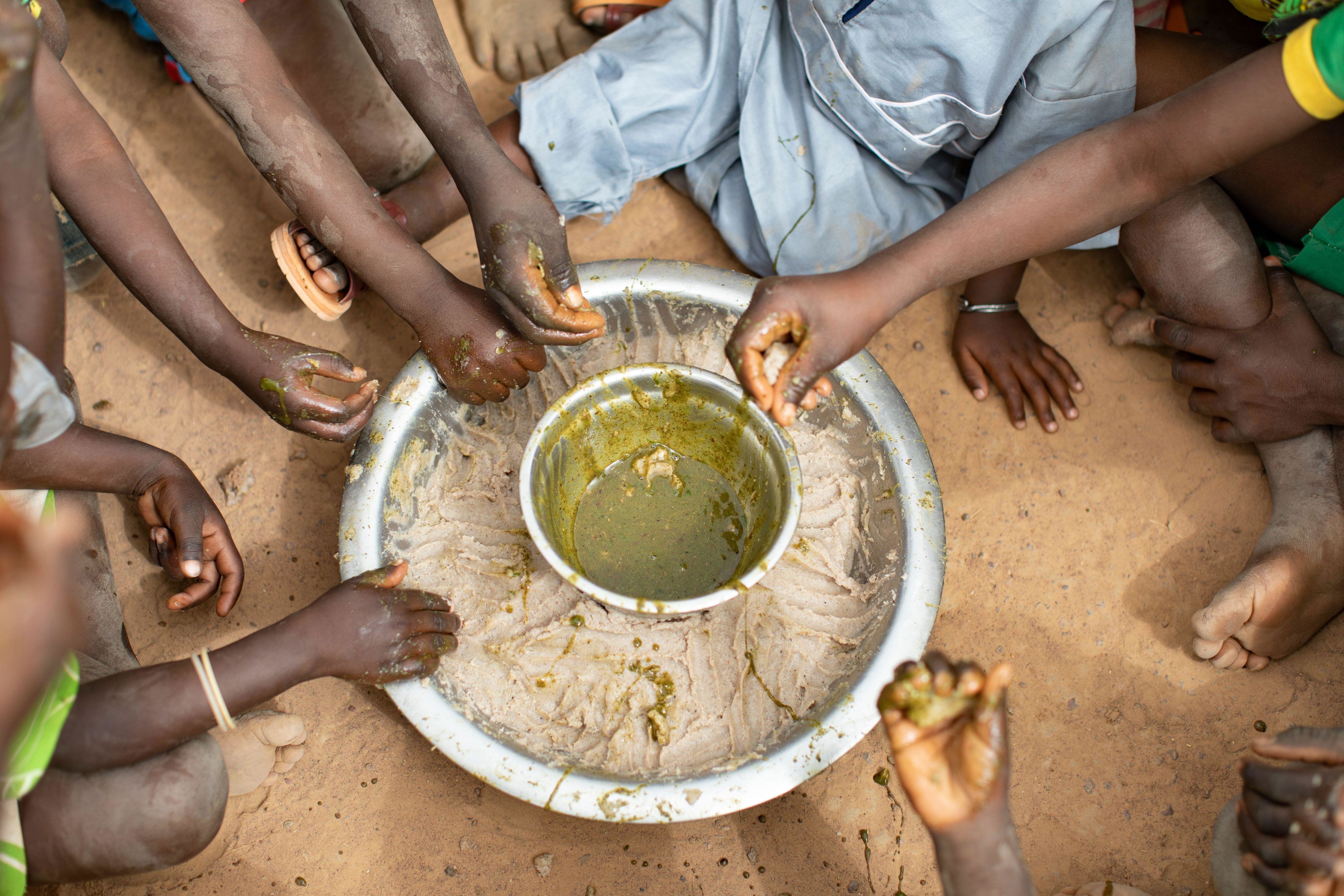 A group of children eat around a communal dish of millet paste and baobab leaf stew