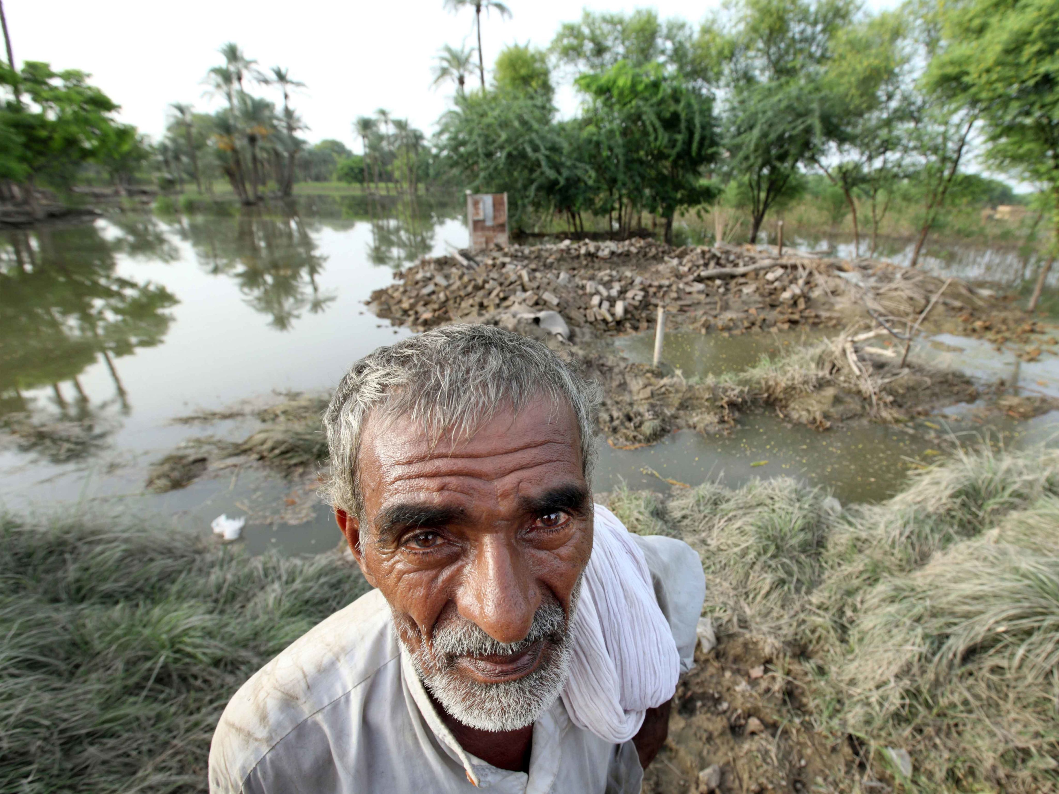 An older man stands in front of his home destroyed by flooding in Pakistan