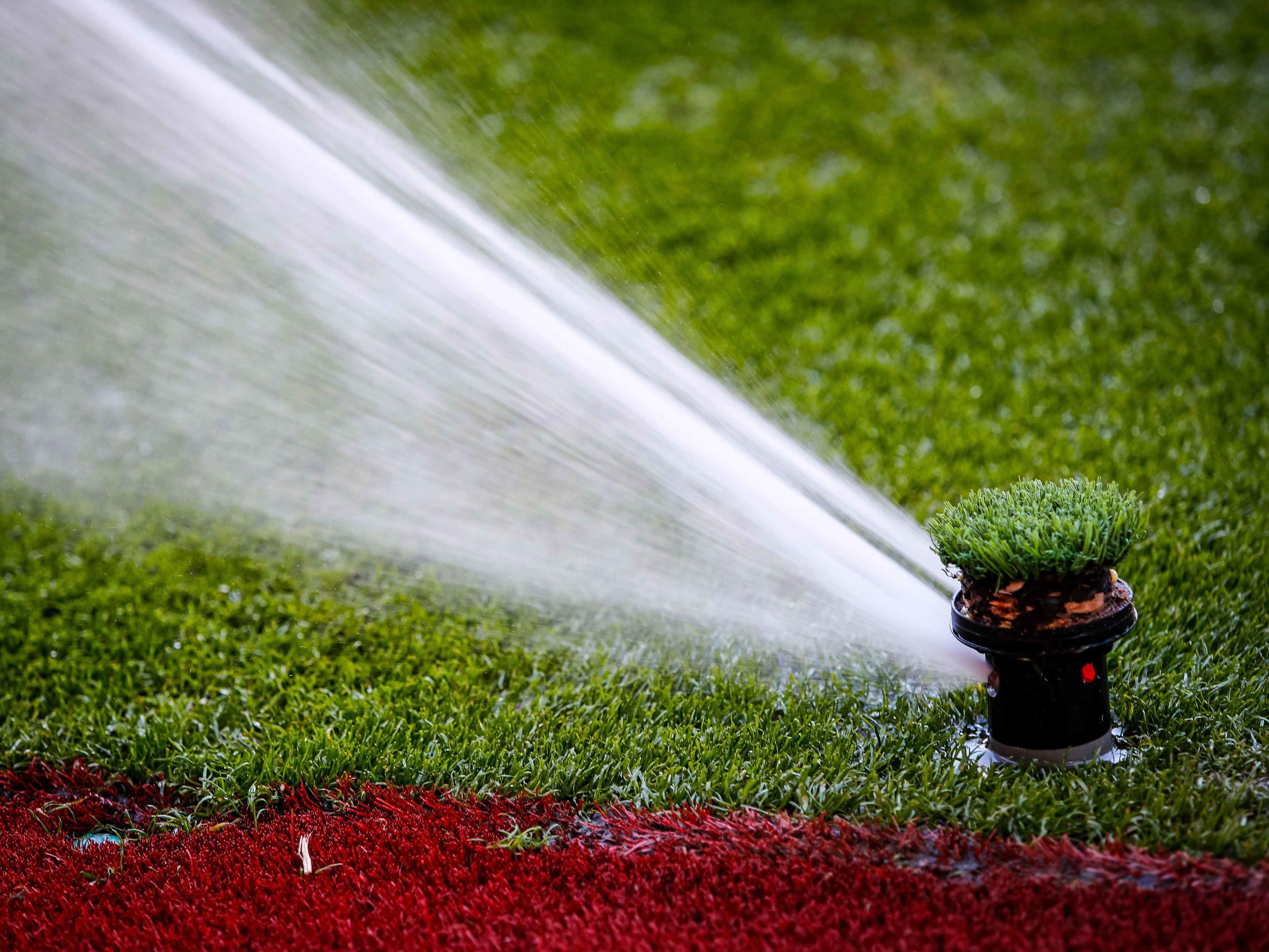 A close up of a sprinkler spraying water on an association football pitch