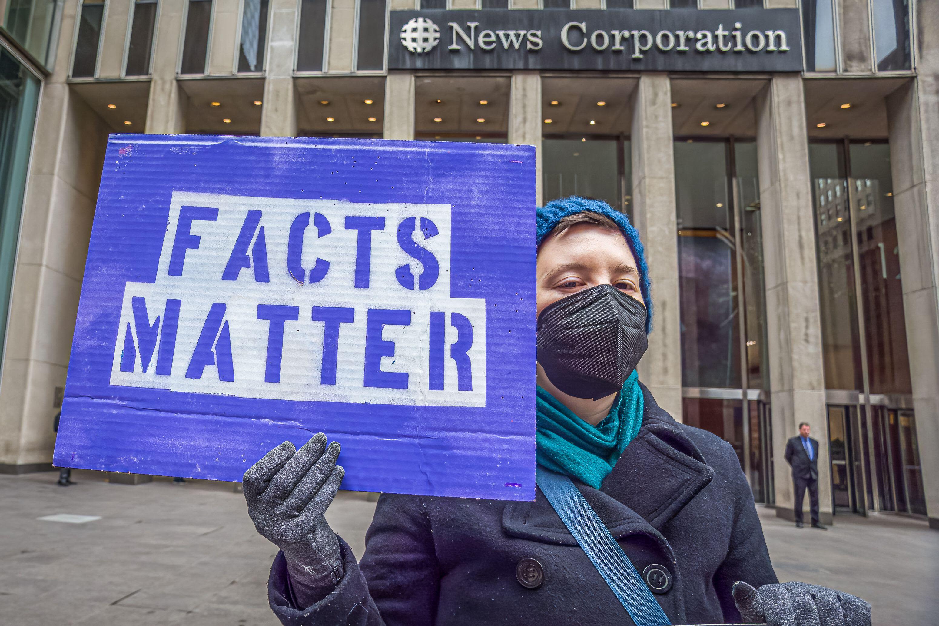 Masked person holding "facts matter" banner