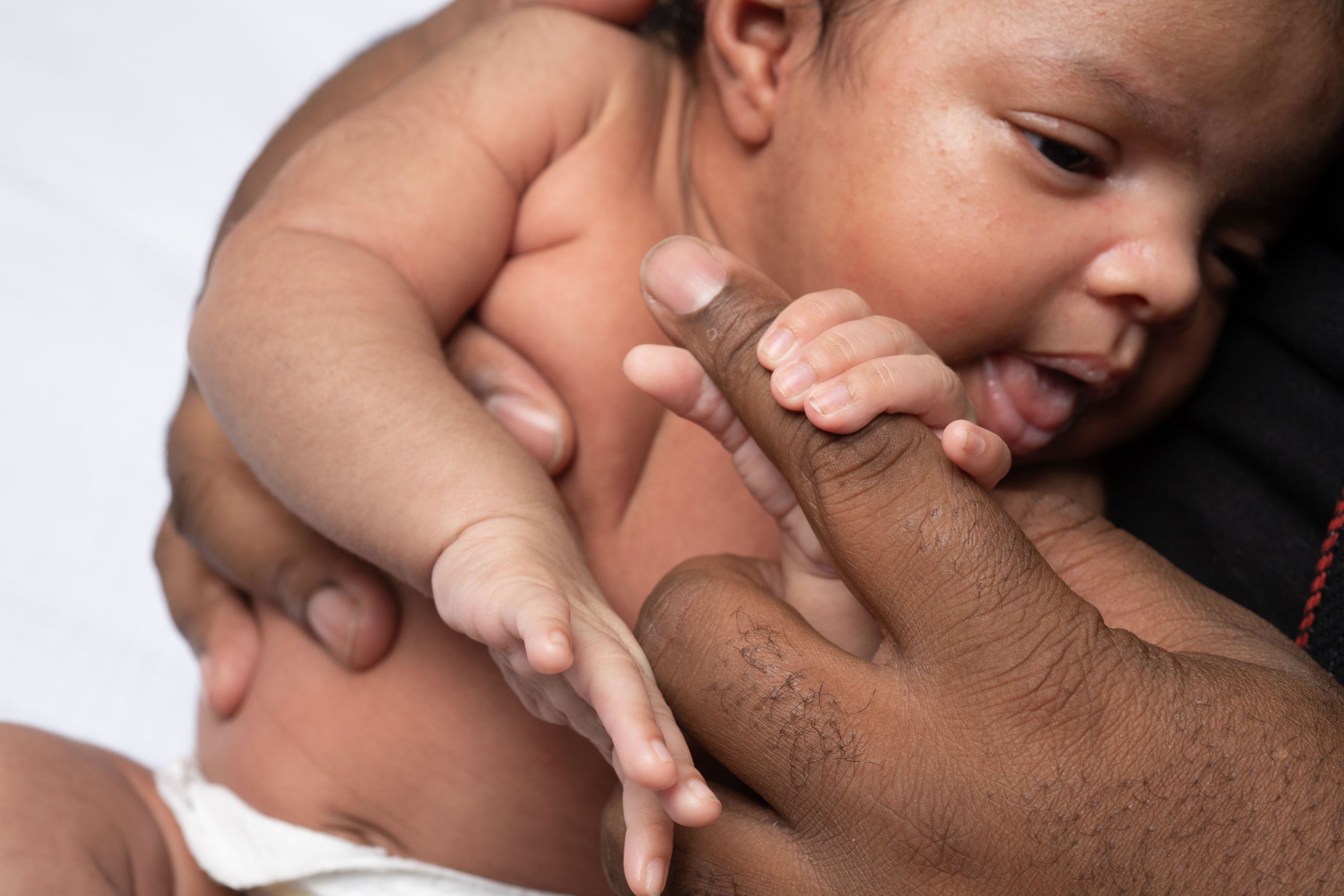 Newborn baby girl 3 weeks old, grasping father's finger, closeup