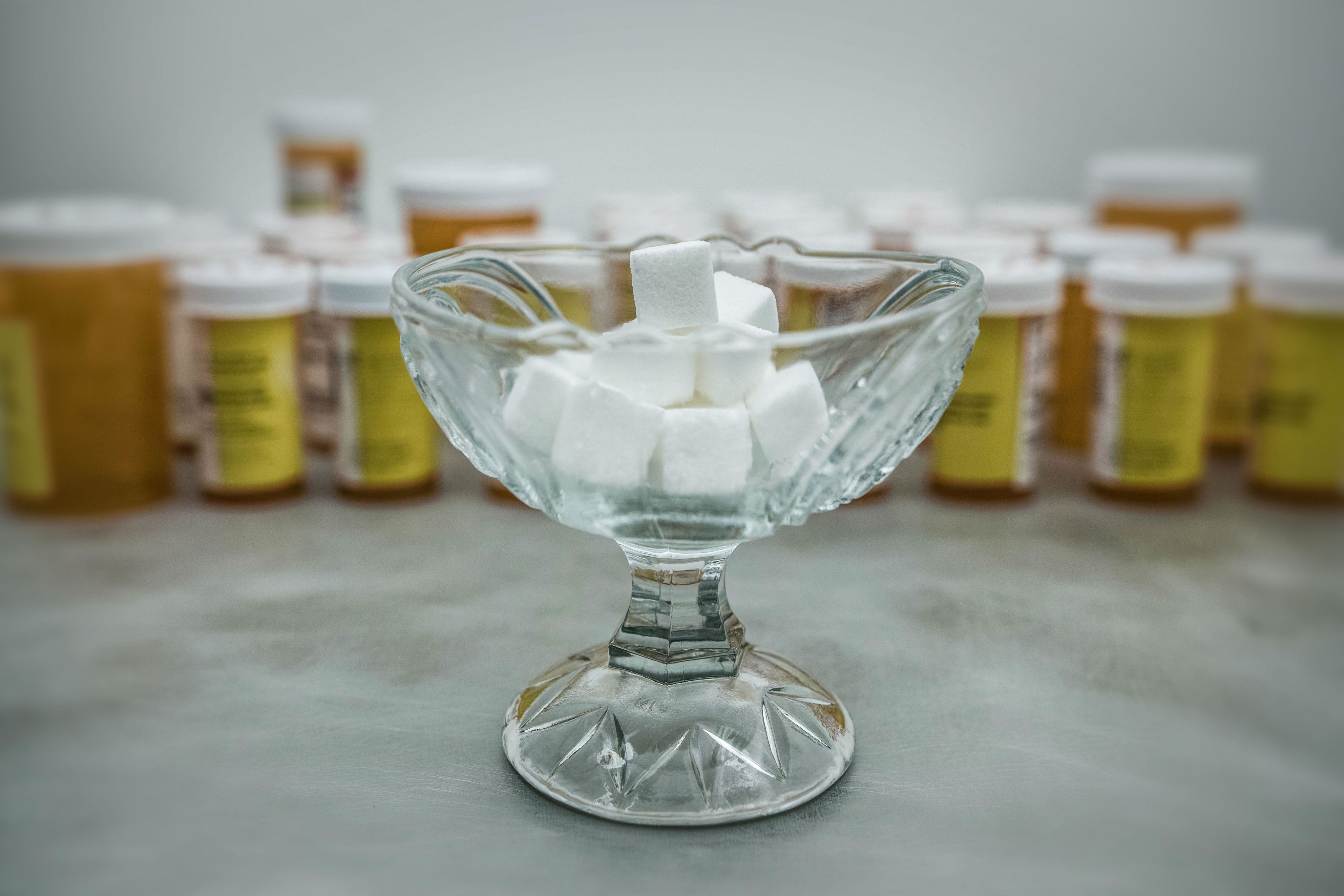 A sugar bowl filled with sugar cubes in front of several prescription medicine containers.