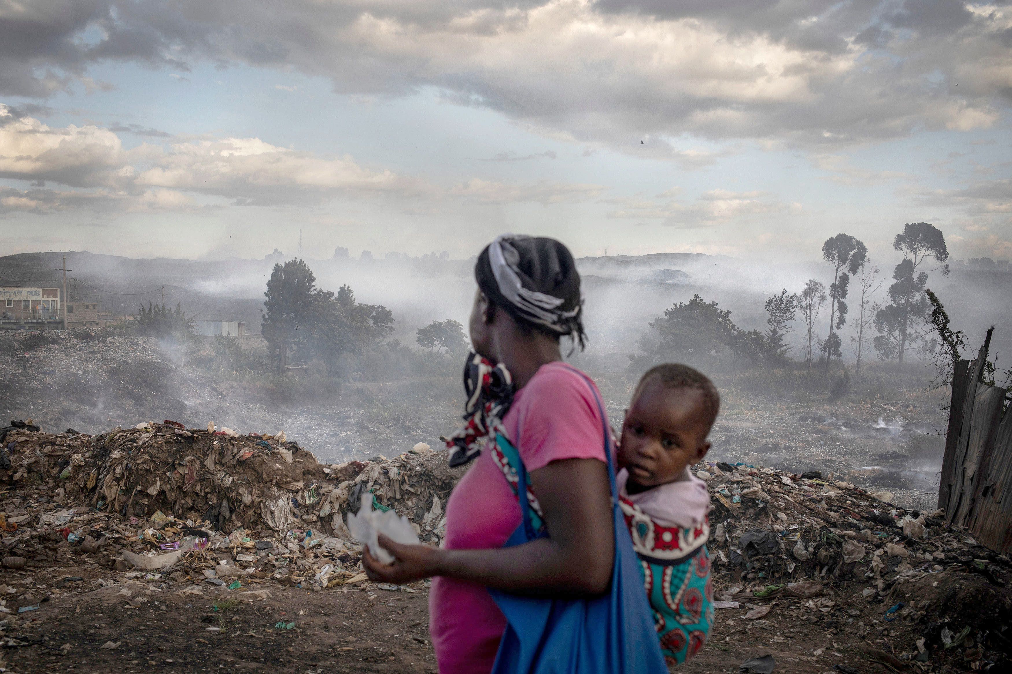 Image of a mother and baby in Africa looking at a rubbish tip