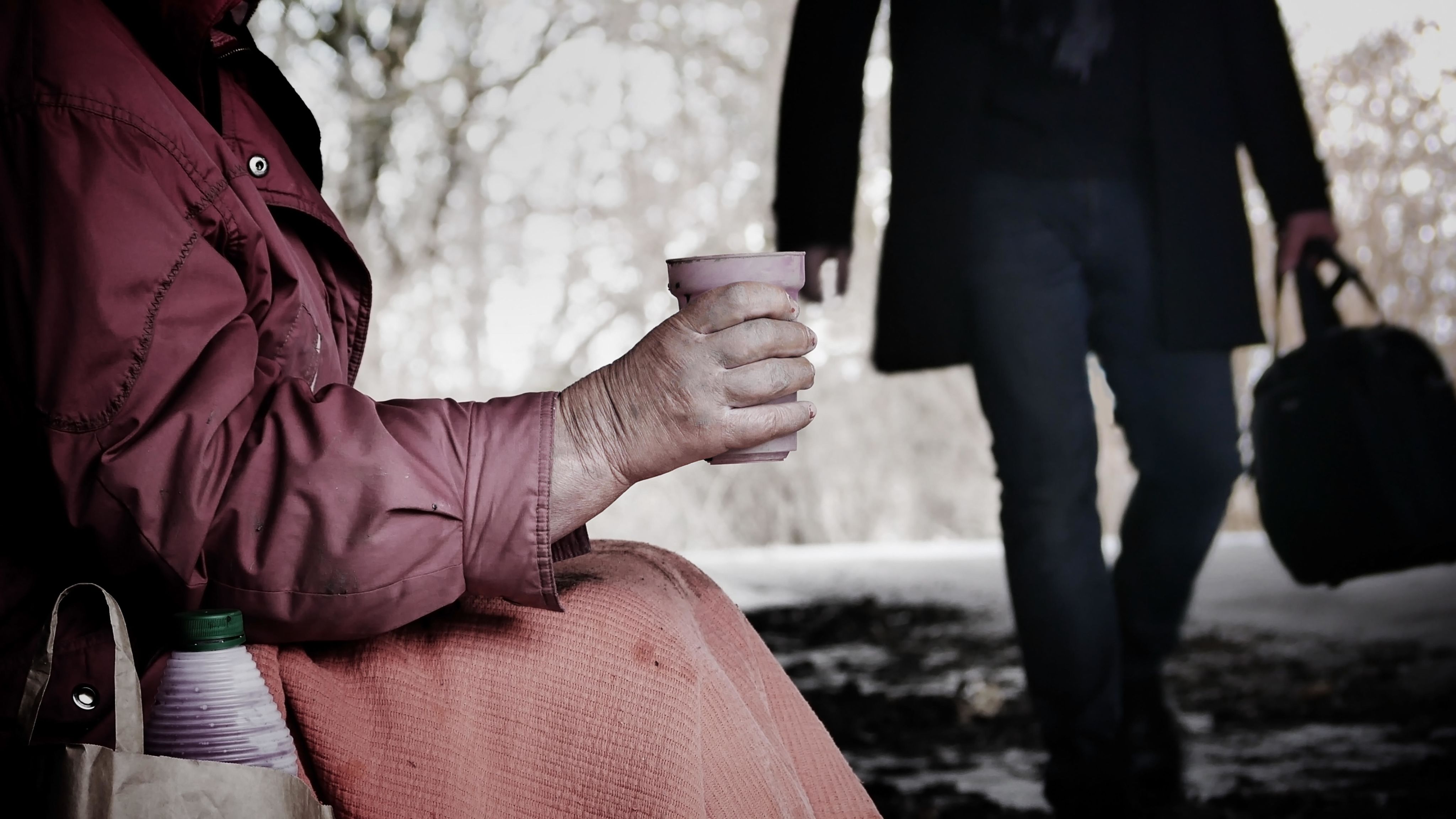 Homeless older woman, holding a cup asking for spare change.