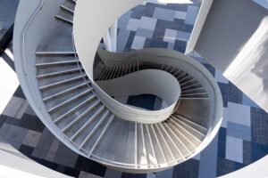 A winding staircase in an ultra modern building, with a blue checkered floor. The overall effect is very abstract.