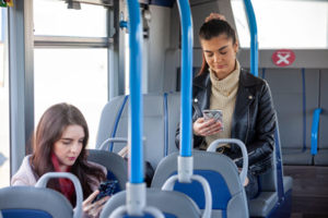 Two college aged women reading their phones on a city bus.