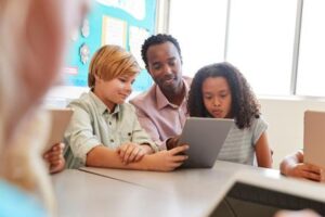 2 children with their teacher looking at a tablet device in a classroom