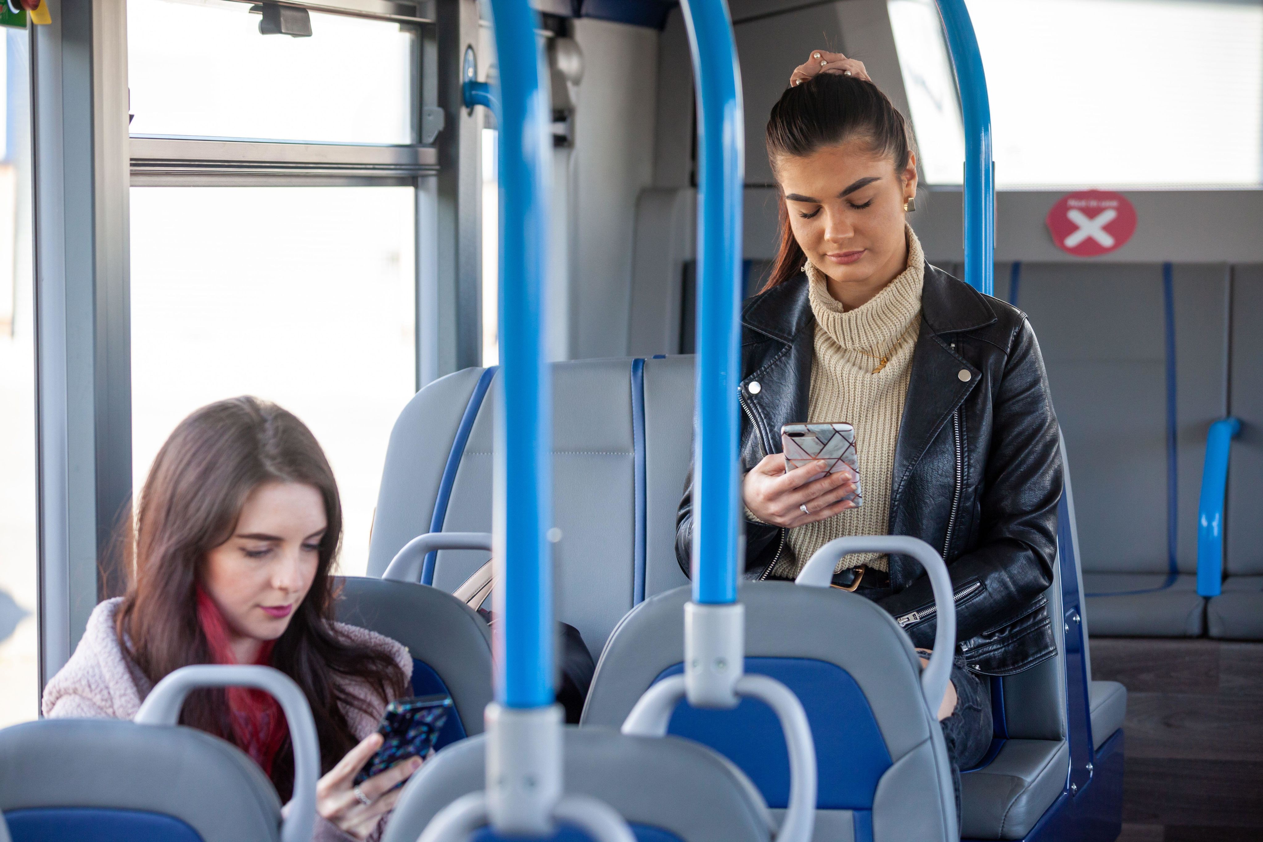 Two women riding public transportation reading eBooks on their phones 