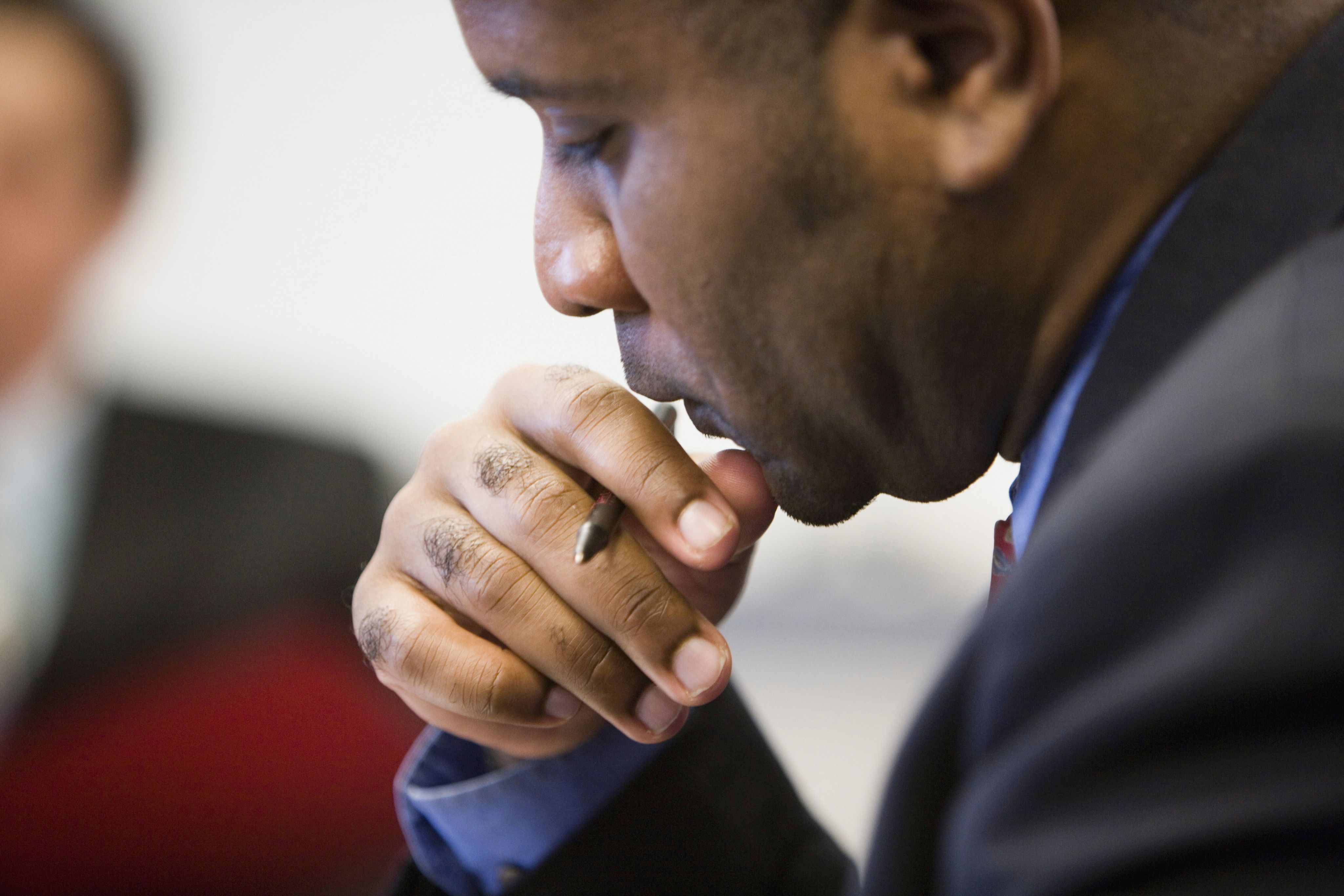 Man of color wearing a suit and holding a pen, contemplating if he will sign something