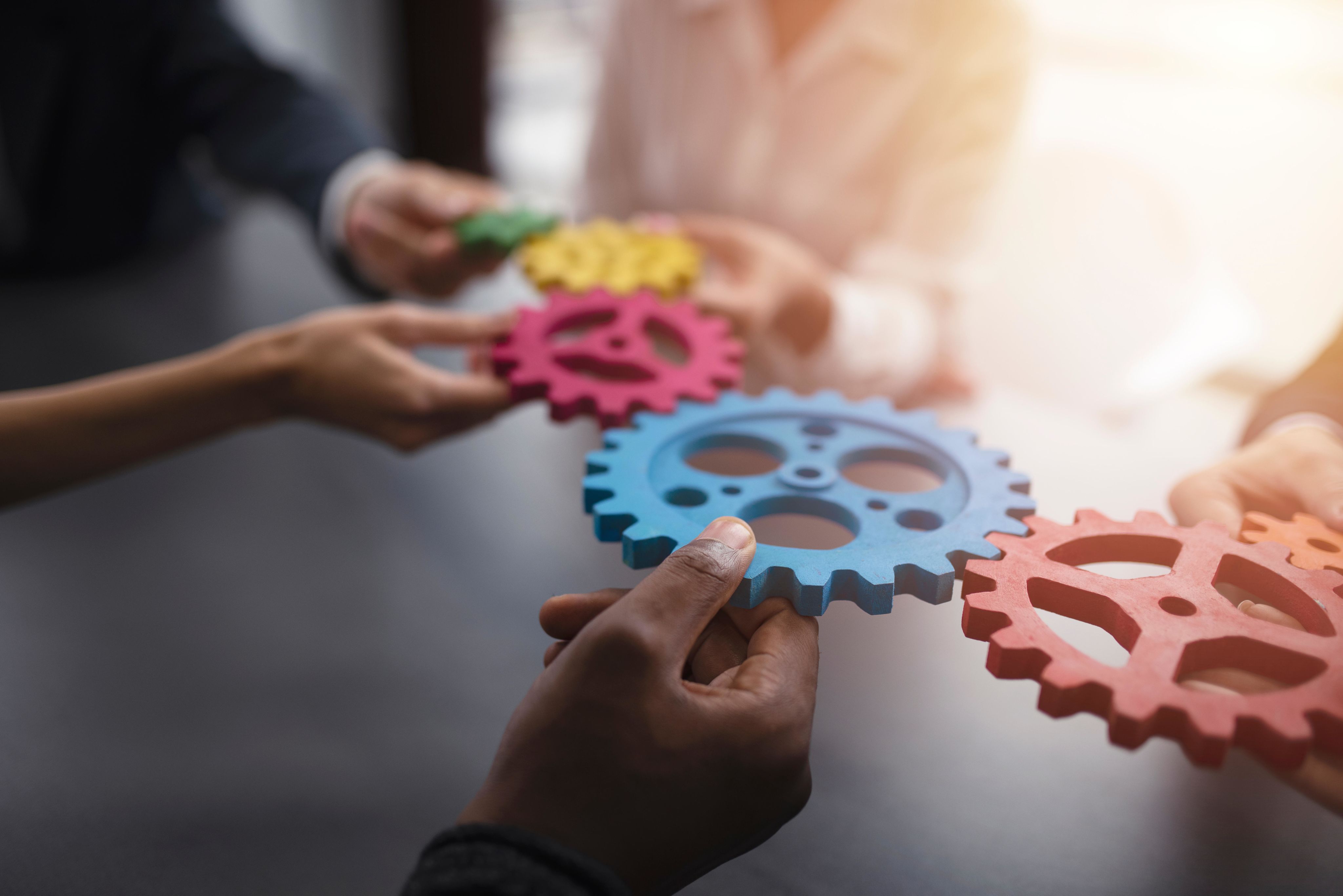 People with different skin colors holding gears of different colors like a puzzle
