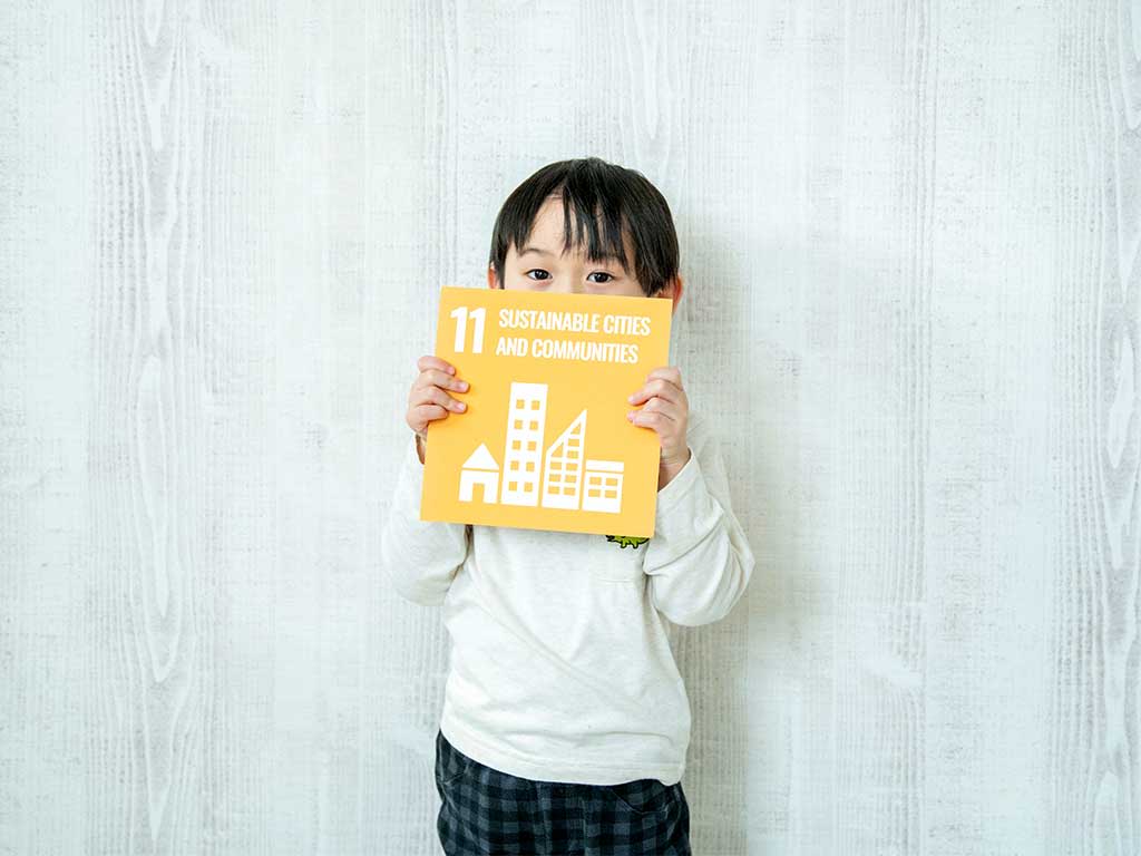 A young boy holds a sign that says "11: Sustainable cities and communities