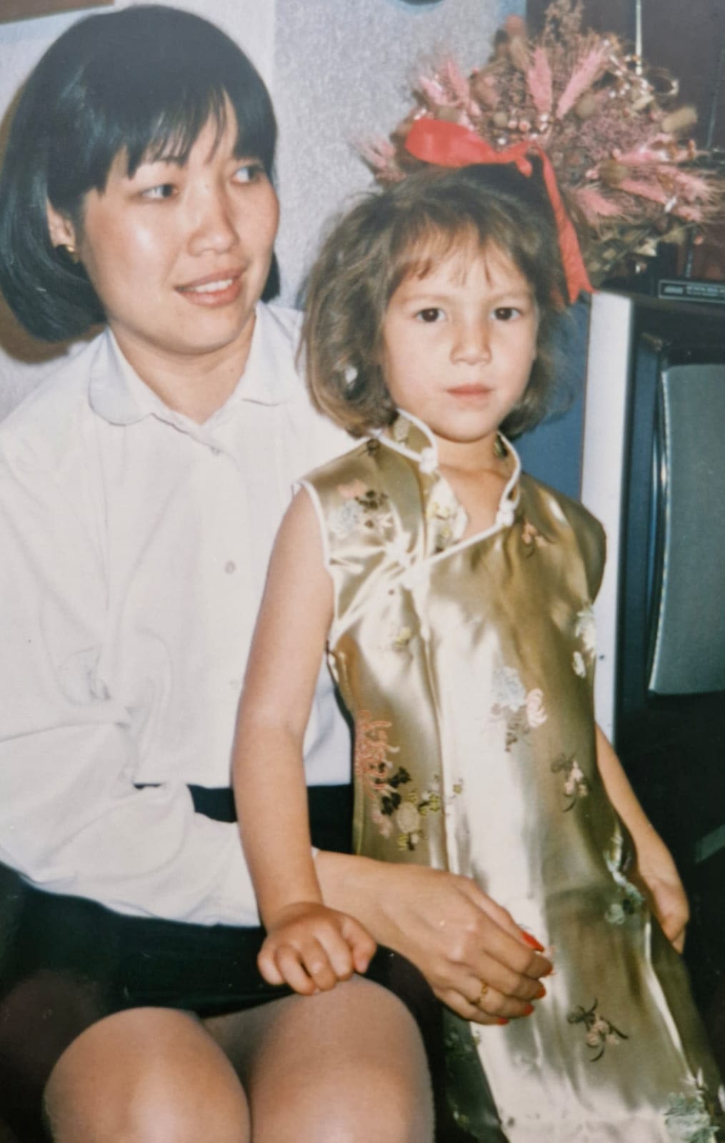 A young Alana Kamp and her mother. Alanna is wearing a gold traditional Asian dress.