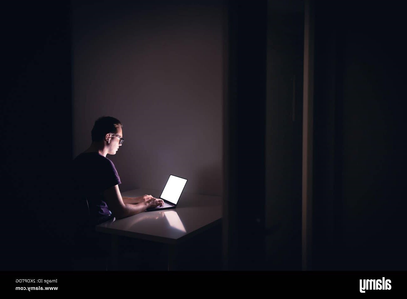 Man with bright laptop screen  in dark room.