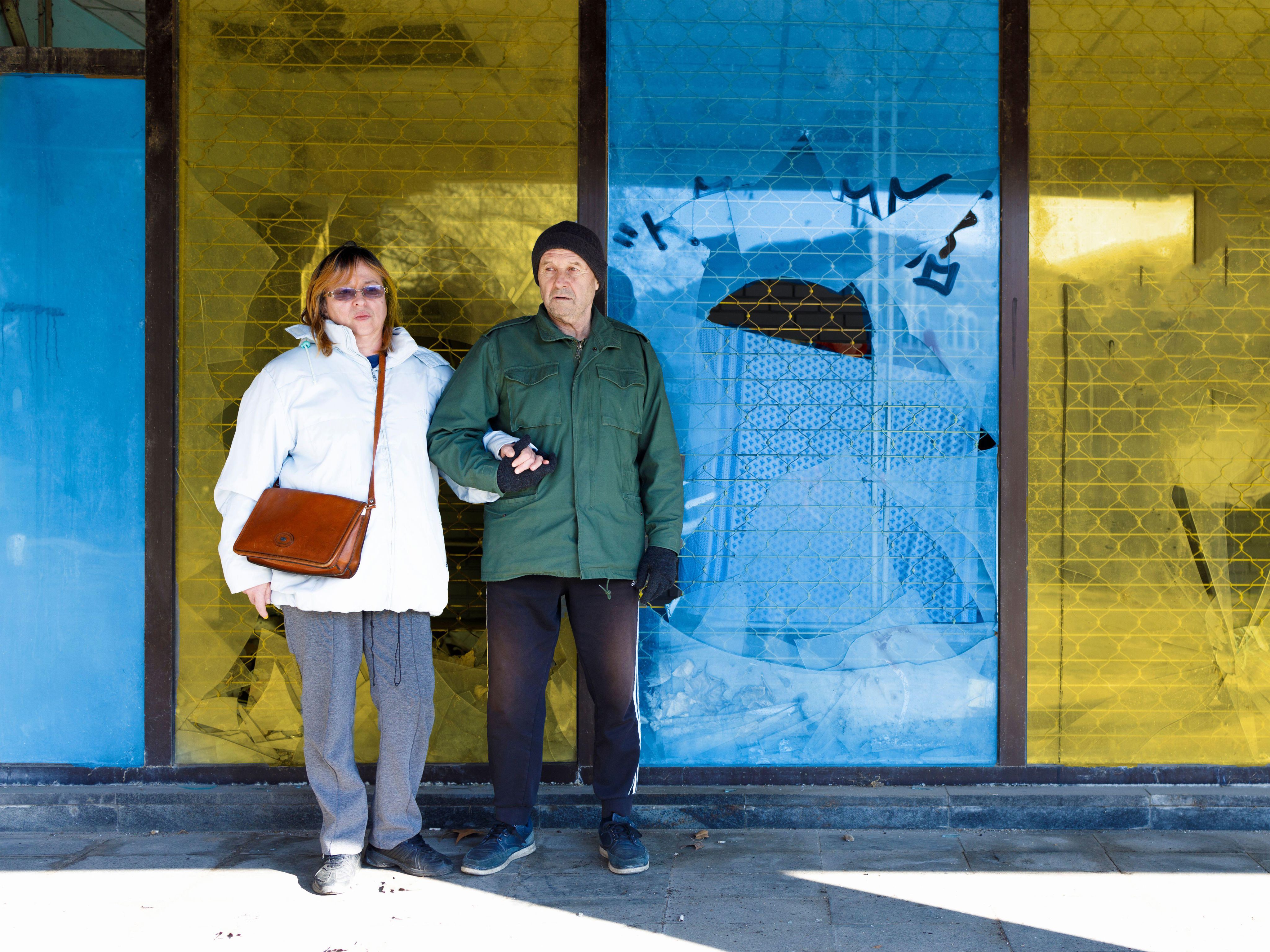 Older Ukrainian couple in front of building in Ukrainian flag colours