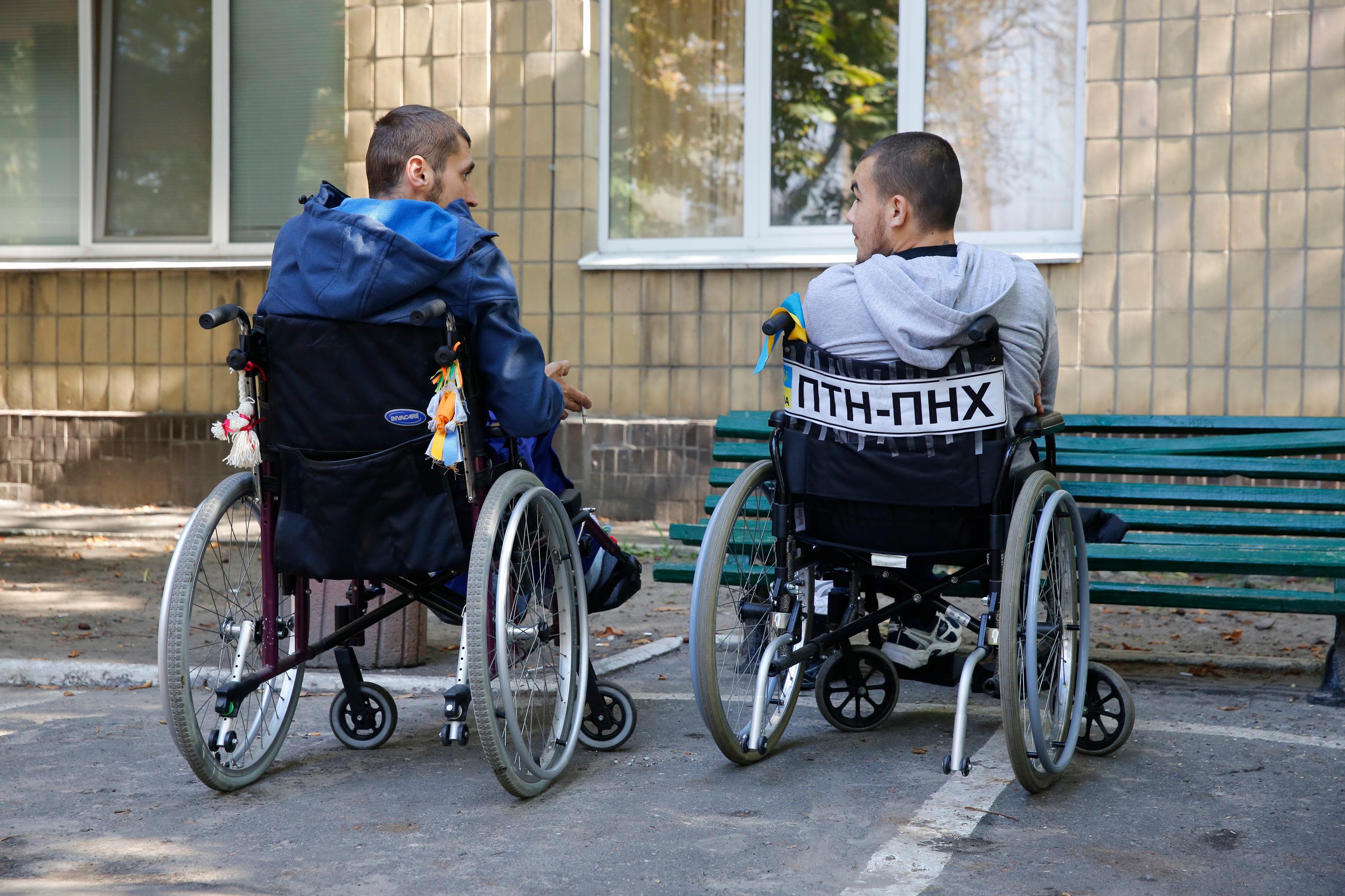 Two people in wheelchairs side by side outside
