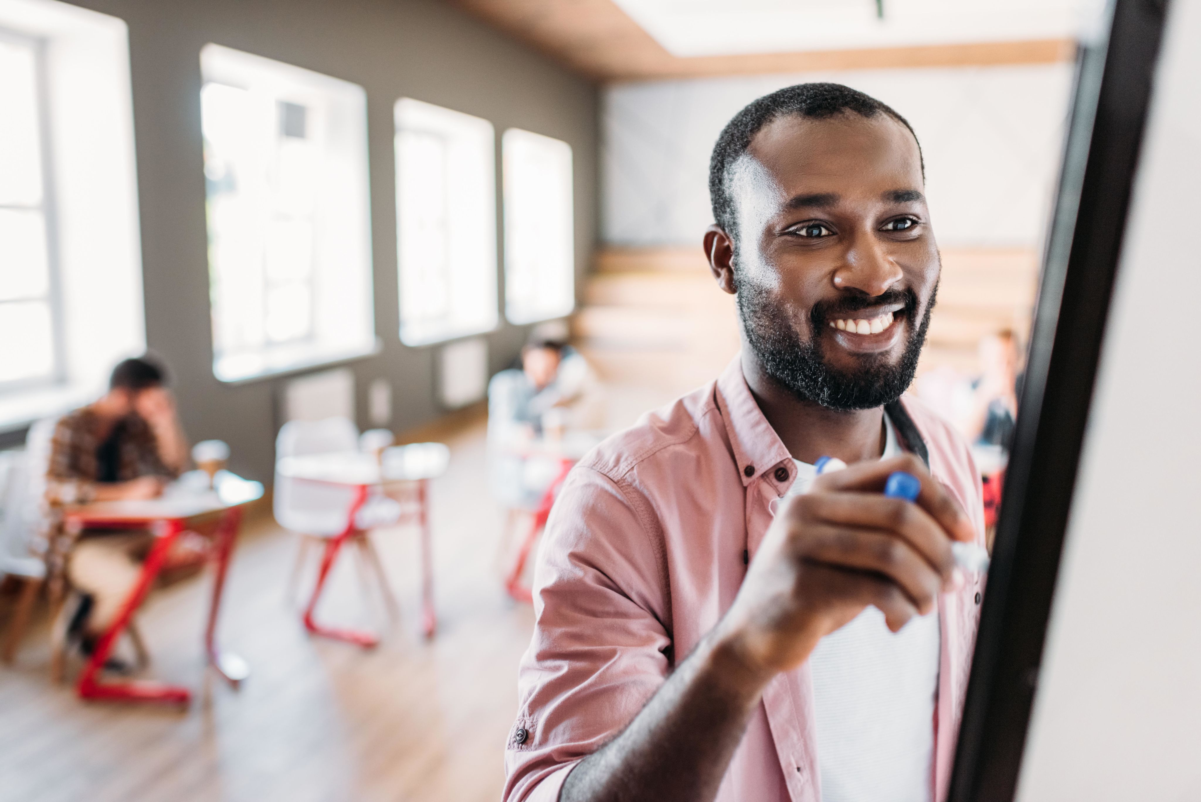Teacher writing on whiteboard with students in background